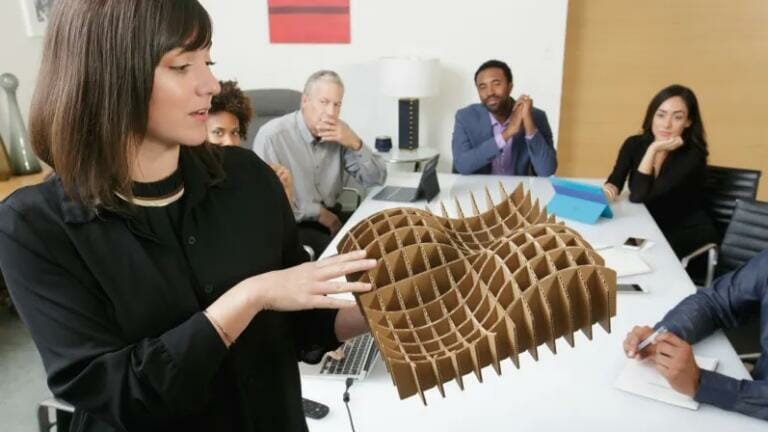 Logitech Group mujer con maqueta en las manos y gente en reunión